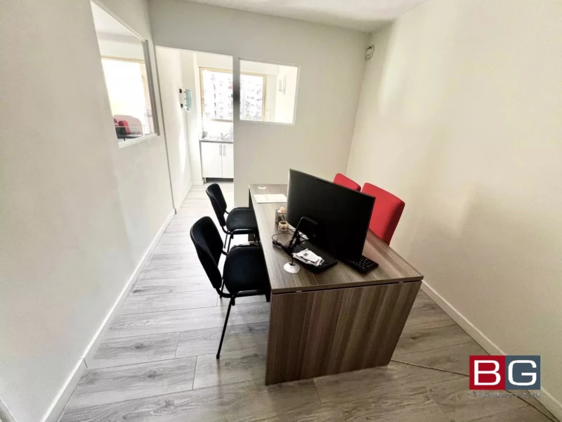 Bureau moderne avec un bureau en bois, deux chaises noires, une chaise rouge, et un ordinateur. Sol en parquet clair.