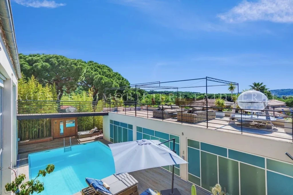Terrasse ensoleillée avec piscine et vue sur la nature verdoyante.