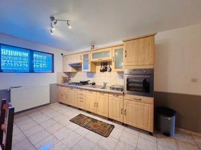 Une cuisine moderne avec des armoires en bois clair, équipée d'un four, d'une cuisinière et d'un évier, sur un sol carrelé beige.