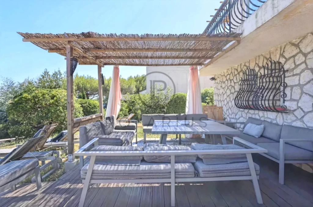 Terrasse ensoleillée avec un salon extérieur, décorée de rideaux et surmontée d'une pergola en bambou.