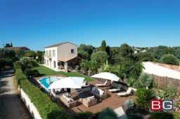Grande maison moderne avec piscine, jardin et terrasse en bois, entourée de végétation luxuriante et vue mer.