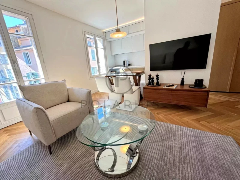 Un salon moderne et lumineux avec un canapé, une table basse en verre, une télévision murale, et une table à manger.