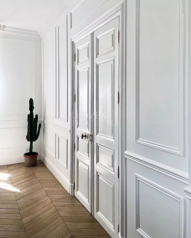Superbes doubles portes moulurées parfaitement intégrées aux boiseries murales, préservant la perspective et le cachet de la bâtisse.