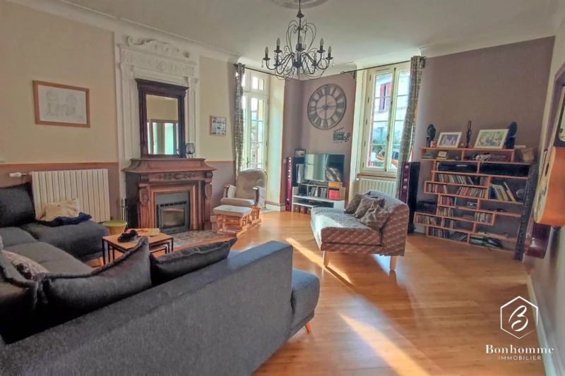 Un salon élégant avec parquet, cheminée, miroir, bibliothèque et un canapé confortable.