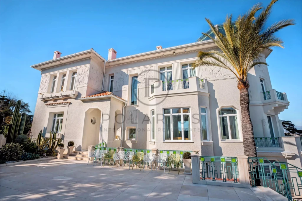 Grande villa élégante avec terrasse, palmiers et ciel bleu.
