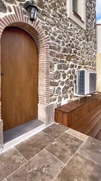 Une entrée secondaire ou annexe pleine de caractère, mariant une lourde porte en bois noble, des murs en pierres apparentes et des menuiseries soignées.