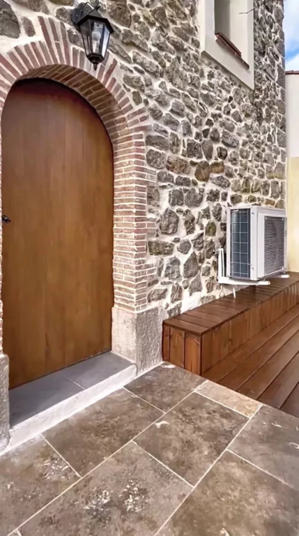 Une entrée secondaire ou annexe pleine de caractère, mariant une lourde porte en bois noble, des murs en pierres apparentes et des menuiseries soignées.