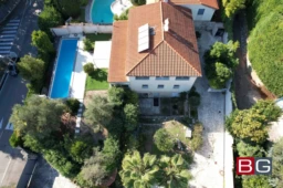 Vue aérienne d'une maison avec un toit en tuiles rouges, entourée de végétation, d'un jardin et de deux piscines.