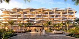 Un bâtiment moderne avec une architecture ondulée se dresse entouré de palmiers, sous un ciel bleu ensoleillé. Des voitures passent devant l'entrée.