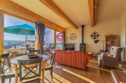 Salon lumineux avec vue panoramique, doté d'un canapé rayé, une table en bois, et un poêle à bois.