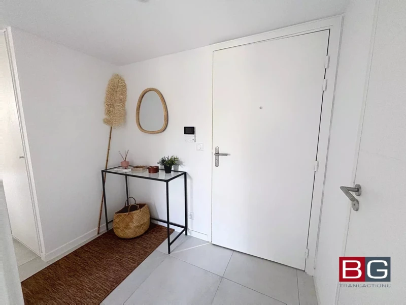 Un hall d'entrée lumineux avec une table console, un miroir, un panier, et une décoration murale.