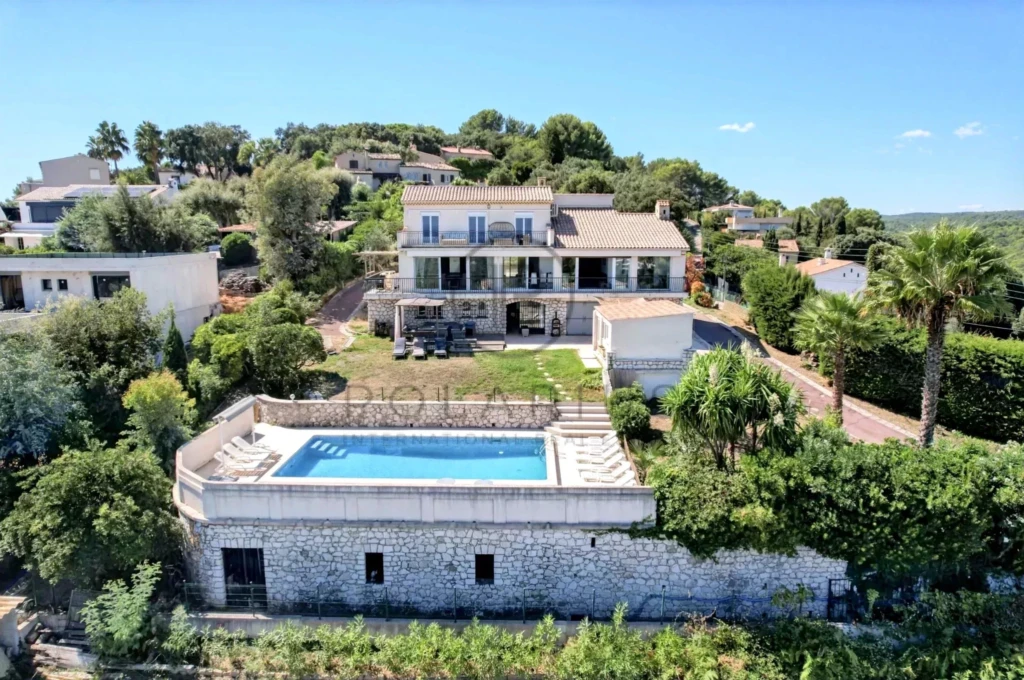 Une villa moderne avec piscine entourée de végétation luxuriante, située sur une colline offrant une vue dégagée.