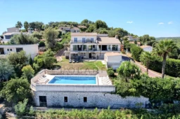 Une villa moderne avec piscine entourée de végétation luxuriante, située sur une colline offrant une vue dégagée.