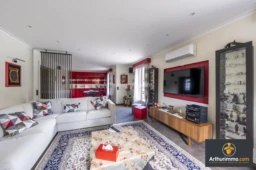Un salon moderne avec un canapé blanc, une télévision murale, et une table basse sur un tapis coloré.