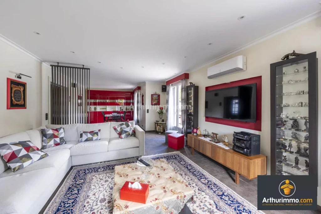Un salon moderne avec un canapé blanc, une télévision murale, et une table basse sur un tapis coloré.