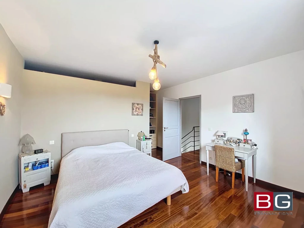 Une chambre lumineuse avec un lit double, un bureau et un parquet en bois.