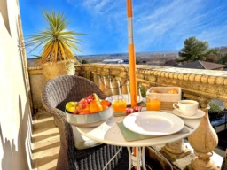 Petit-déjeuner sur un balcon ensoleillé avec fruits, jus d'orange et viennoiseries.