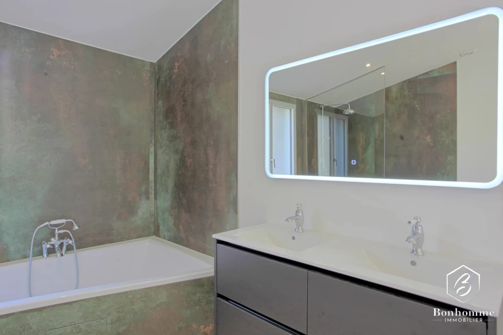 Une salle de bain moderne avec une baignoire, un grand miroir rétroéclairé et un double lavabo.