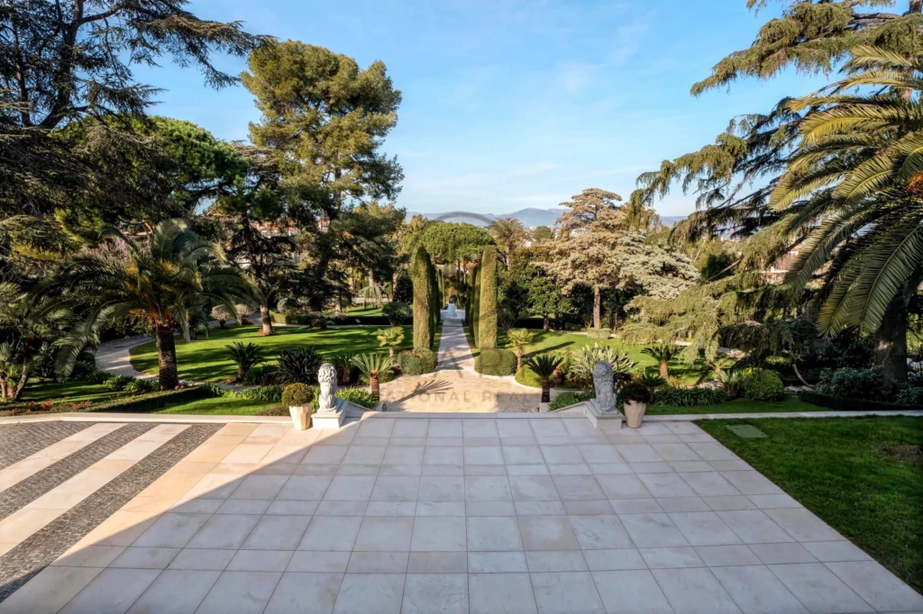 Une terrasse en marbre avec vue sur un jardin verdoyant et des arbres majestueux sous un ciel bleu.
