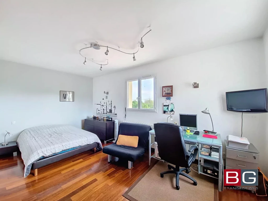 Une chambre lumineuse avec un lit, un bureau, et une chaise, sur un sol en bois.