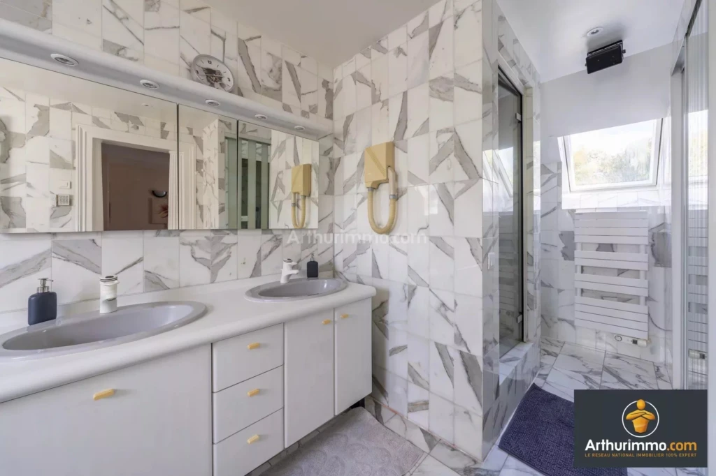 MOULIGNON salle de bain moderne avec un double lavabo, des murs et un sol en marbre, ainsi qu'une douche avec paroi vitrée.