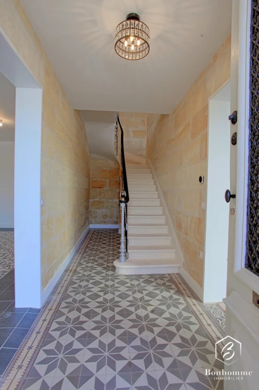 Entrée lumineuse avec un escalier blanc et un sol carrelé à motifs géométriques.