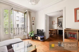Salon lumineux avec parquet en bois et accès au balcon.