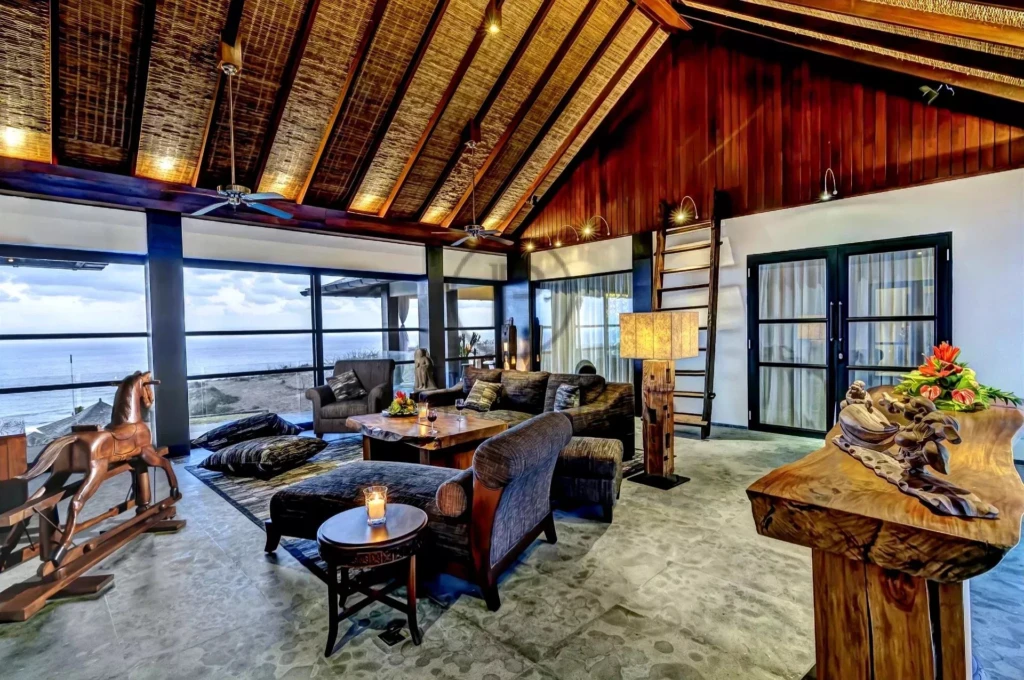 Un salon spacieux avec un plafond en bois incliné, des meubles confortables et une vue sur la mer à travers de grandes baies vitrées.