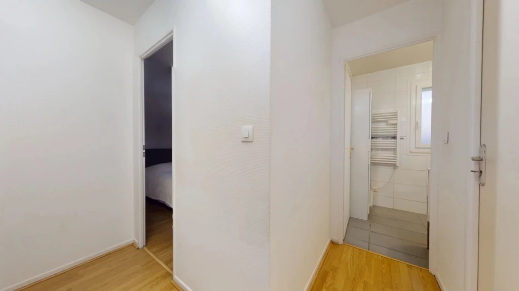 Un couloir avec parquet menant à deux pièces, dont l'une semble être une chambre.