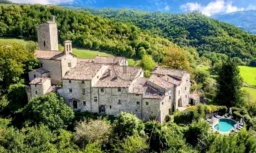 Un château ancien entouré de verdure luxuriante avec une piscine, niché dans un paysage vallonné.