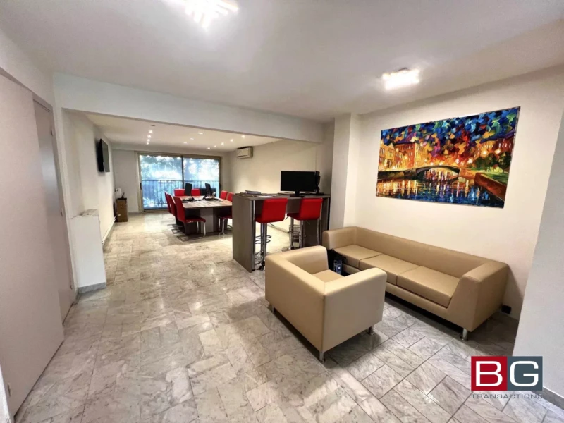 Une pièce moderne avec un canapé beige, des chaises rouges autour d'une table et une peinture colorée sur le mur.