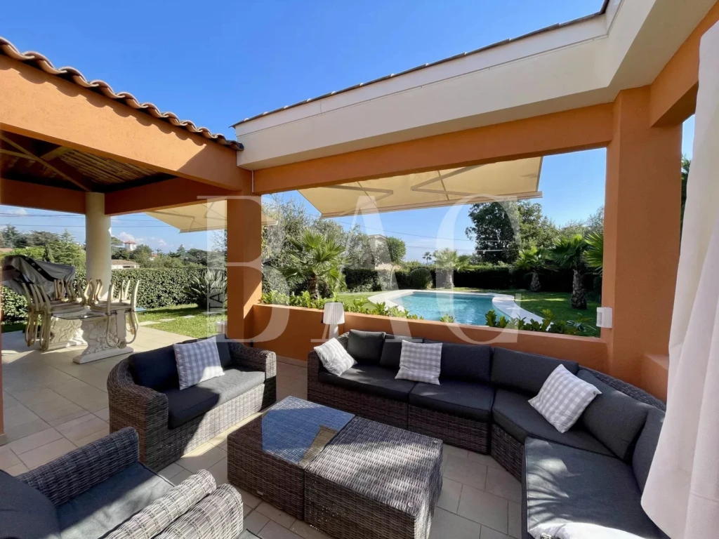 Salon extérieur élégant avec vue sur une piscine et un jardin verdoyant.