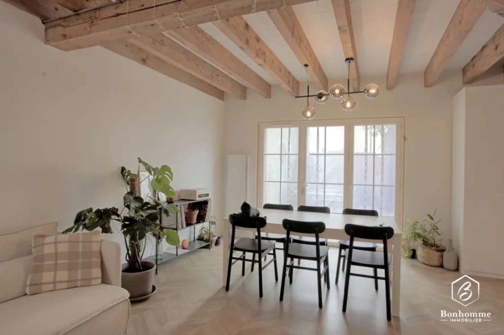 Salle à manger lumineuse avec poutres en bois apparentes et grande fenêtre.