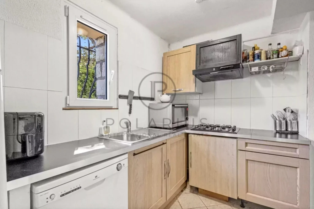 Petite cuisine moderne avec éléments en bois, électroménagers, et fenêtre avec vue sur l'extérieur.