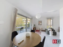 Une pièce lumineuse avec un coin salle à manger, un canapé, et un balcon visible par une grande porte-fenêtre.