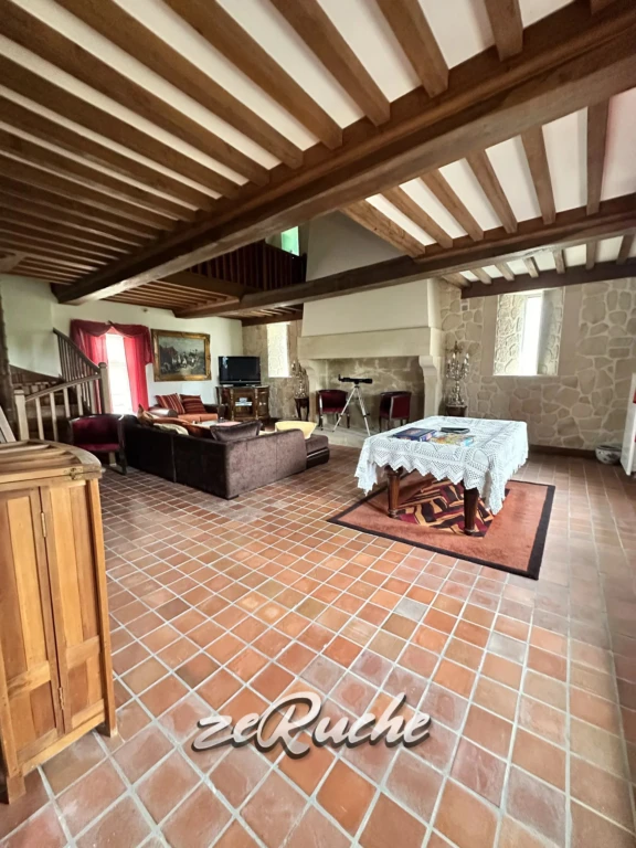 Salon spacieux avec poutres en bois apparentes et cheminée en pierre.