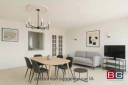 Un salon moderne et épuré avec une table à manger et des chaises noires, un canapé gris, une télévision et des murs décorés de tableaux.