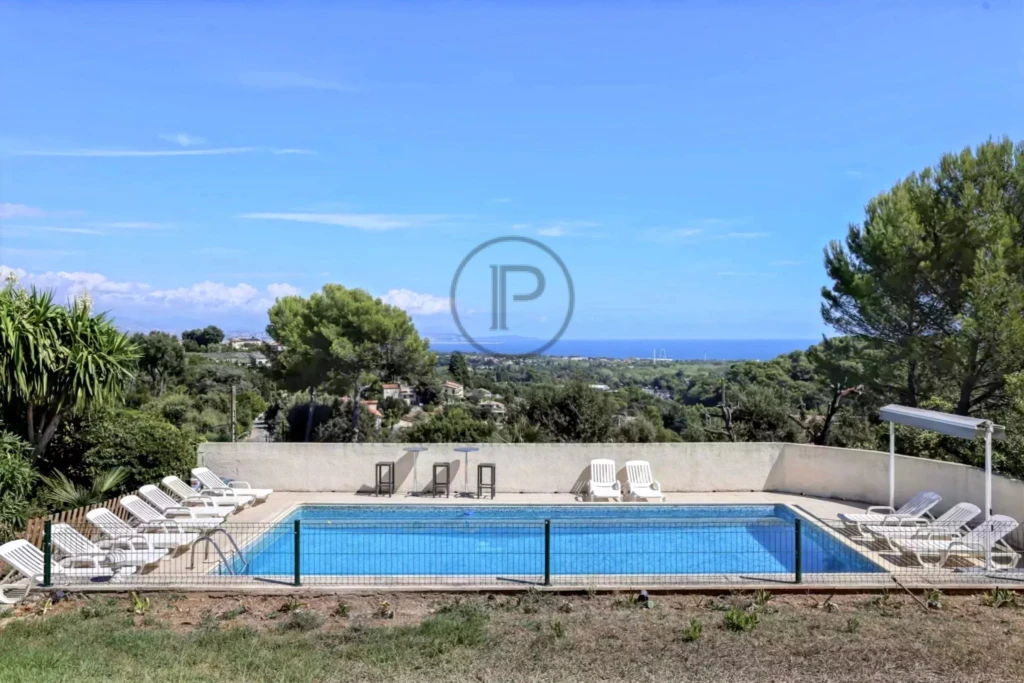 Piscine entourée de transats, avec vue sur la mer et la végétation environnante.