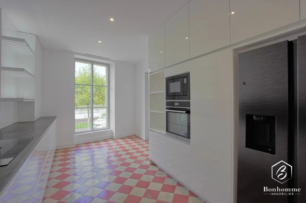 Cuisine moderne avec un sol à carreaux rouges et blancs, grandes fenêtres, et électroménagers intégrés.