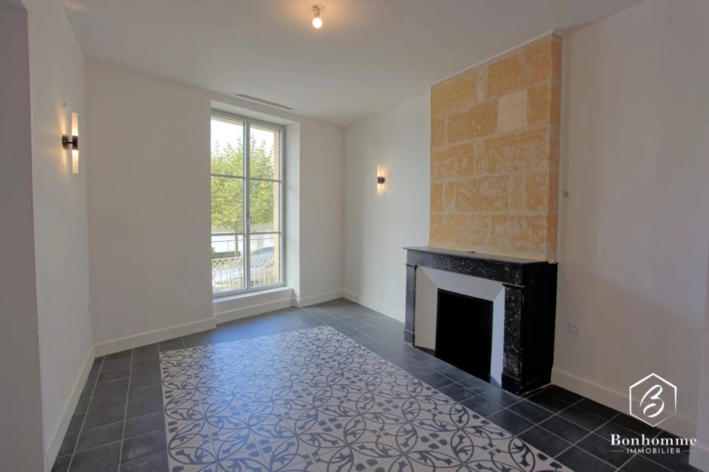 Une pièce lumineuse avec un sol en carrelage décoratif, une cheminée moderne et une grande fenêtre donnant sur l'extérieur.