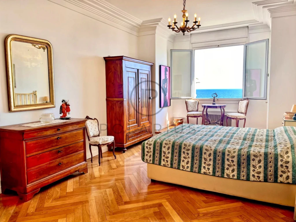 Chambre lumineuse avec vue sur la mer, mobilier en bois élégant, parquet en chêne, et décoration classique.