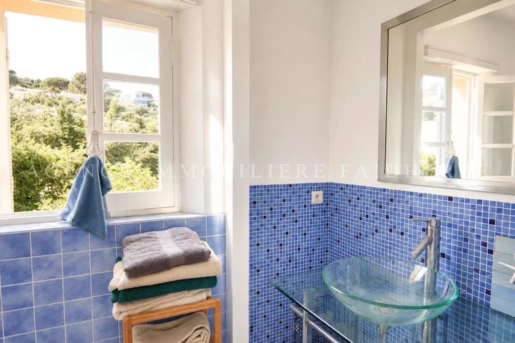 Belle salle de bain lumineuse avec fenêtre et mosaïque bleue.