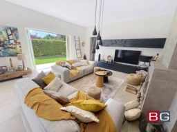Un salon moderne et lumineux avec des canapés confortables, des coussins colorés, une grande télévision, et une porte ouverte sur un jardin.