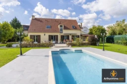 Maison moderne avec piscine, terrasse et jardin, sous un ciel bleu.