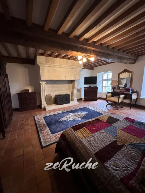 Charmante salle de séjour avec cheminée en pierre et plafond en poutres apparentes.