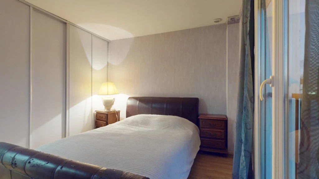 Une chambre avec un lit, une lampe sur une table de chevet et des rideaux à la fenêtre.