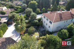 Vue aérienne d'une grande maison entourée de verdure et d'arbres, avec un toit en tuiles rouges et un jardin spacieux.