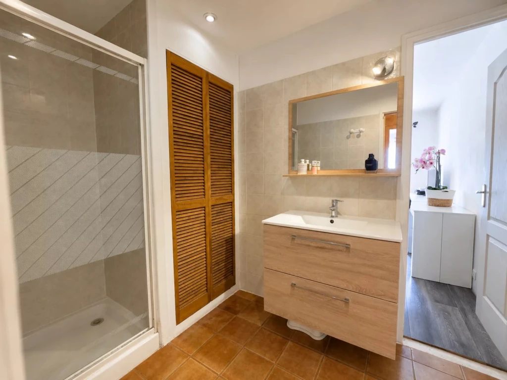 Une salle d'eau moderne équipée d'une cabine de douche, d'un meuble vasque suspendu et de rangements intégrés.