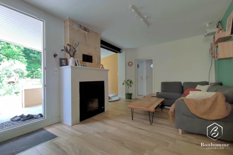 Un salon moderne avec une cheminée, canapé gris, table basse en bois, et des portes-fenêtres donnant sur un espace extérieur.