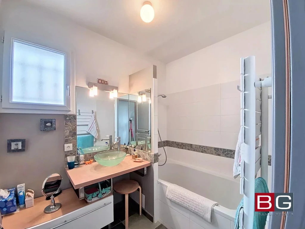 Une salle de bain moderne avec une baignoire, un lavabo en verre, et un miroir éclairé.